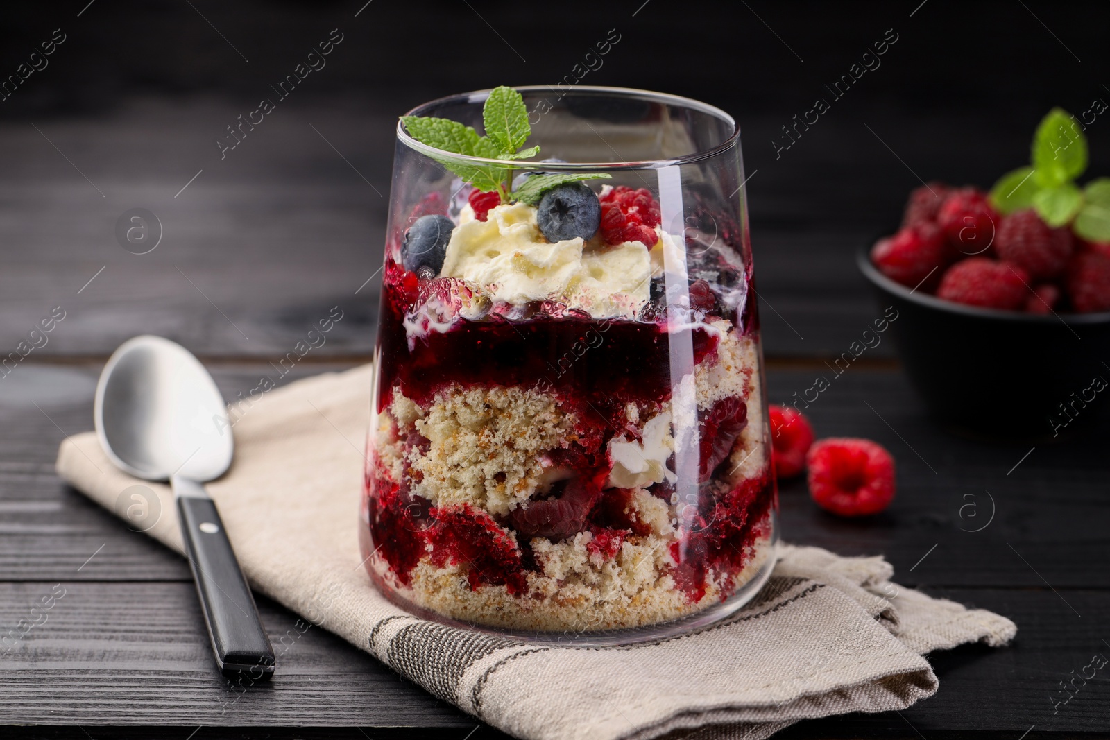 Photo of Tasty trifle dessert. Berries, sponge cake and whipped cream in glass on black wooden table