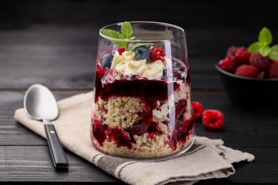 Photo of Tasty trifle dessert. Berries, sponge cake and whipped cream in glass on black wooden table