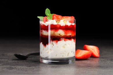 Photo of Tasty trifle dessert. Strawberries, sponge cake and whipped cream in glass on grey table