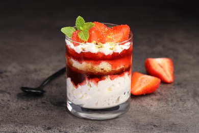 Photo of Tasty trifle dessert. Strawberries, sponge cake and whipped cream in glass on grey table