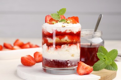 Photo of Tasty trifle dessert. Strawberries, sponge cake and whipped cream in glass on beige table