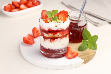 Photo of Tasty trifle dessert. Strawberries, sponge cake and whipped cream in glass on beige table