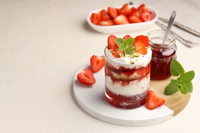 Photo of Tasty trifle dessert. Strawberries, sponge cake and whipped cream in glass on beige table, space for text