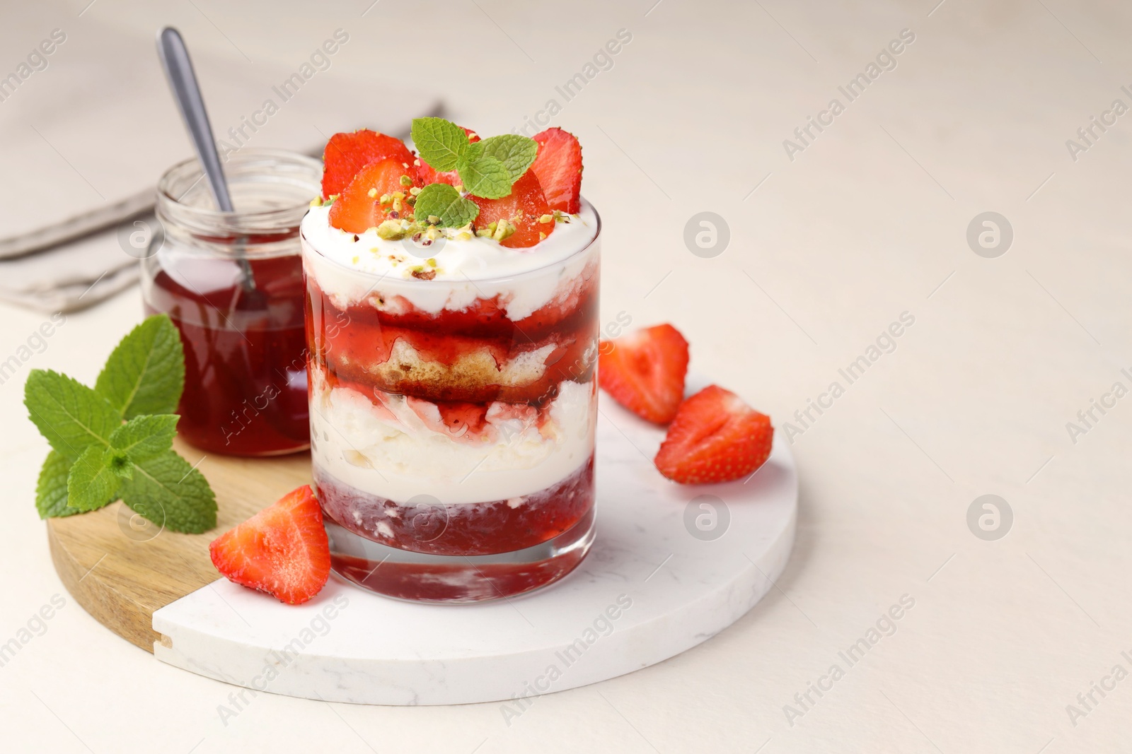 Photo of Tasty trifle dessert. Strawberries, sponge cake and whipped cream in glass on beige table, space for text