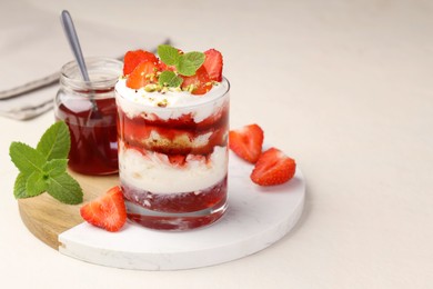 Photo of Tasty trifle dessert. Strawberries, sponge cake and whipped cream in glass on beige table, space for text