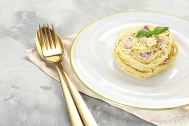 Photo of Plate with delicious pasta Carbonara and cutlery on grey textured table, closeup