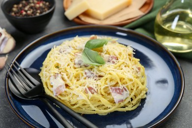 Photo of Plate with delicious pasta Carbonara and cutlery on grey textured table, closeup