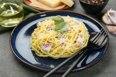 Photo of Plate with delicious pasta Carbonara and cutlery on grey textured table, closeup