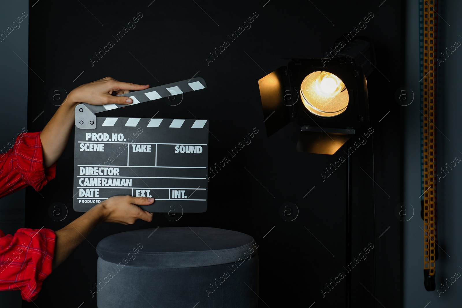 Photo of Woman with clapperboard near spotlight on black background, closeup