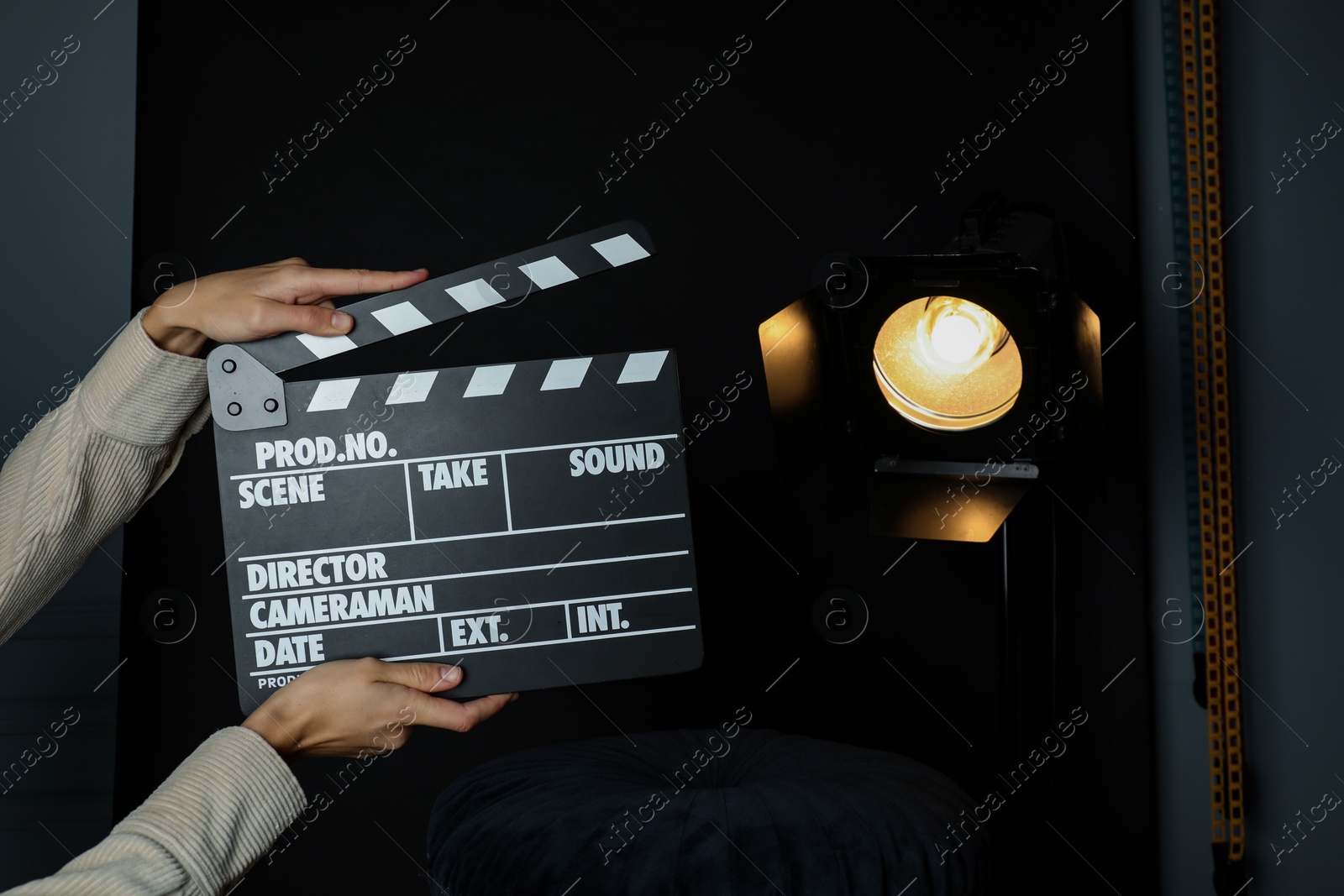 Photo of Woman with clapperboard near spotlight on black background, closeup