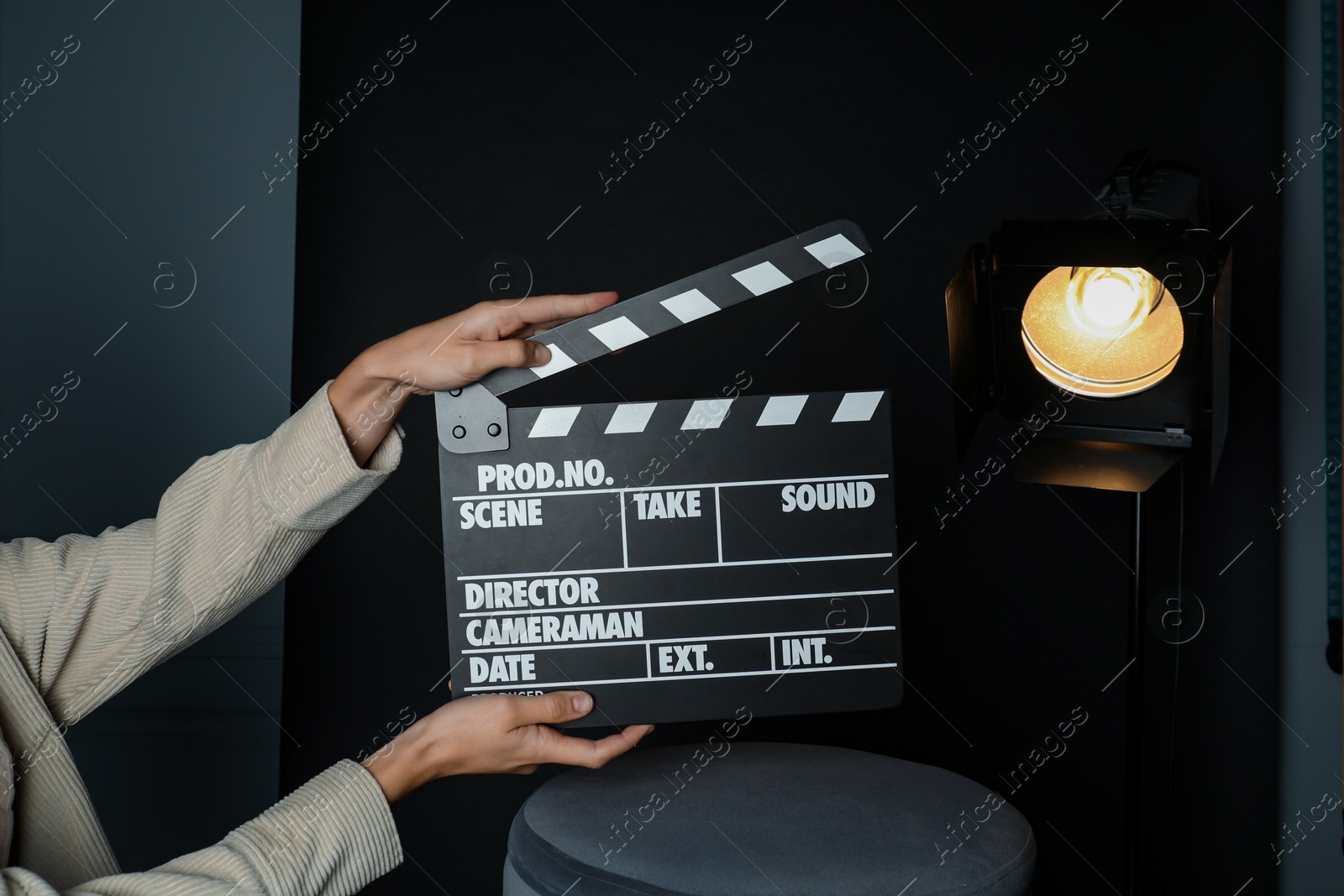 Photo of Woman with clapperboard near spotlight on black background, closeup