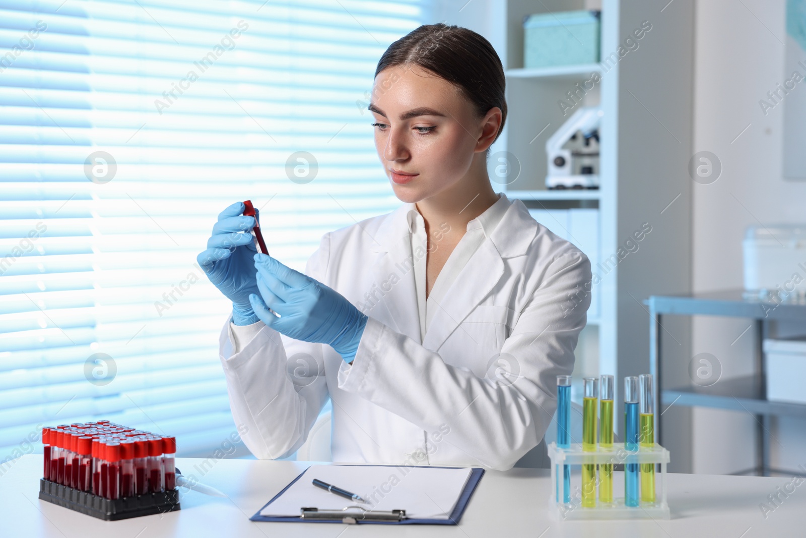 Photo of Laboratory testing. Doctor holding test tube with blood sample at table indoors