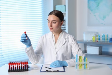 Photo of Laboratory testing. Doctor holding test tube with blood sample at table indoors