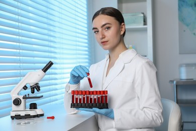 Photo of Laboratory testing. Doctor taking test tube with blood sample from rack indoors