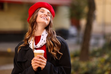 Photo of Stylish woman with cup of hot drink outdoors, space for text