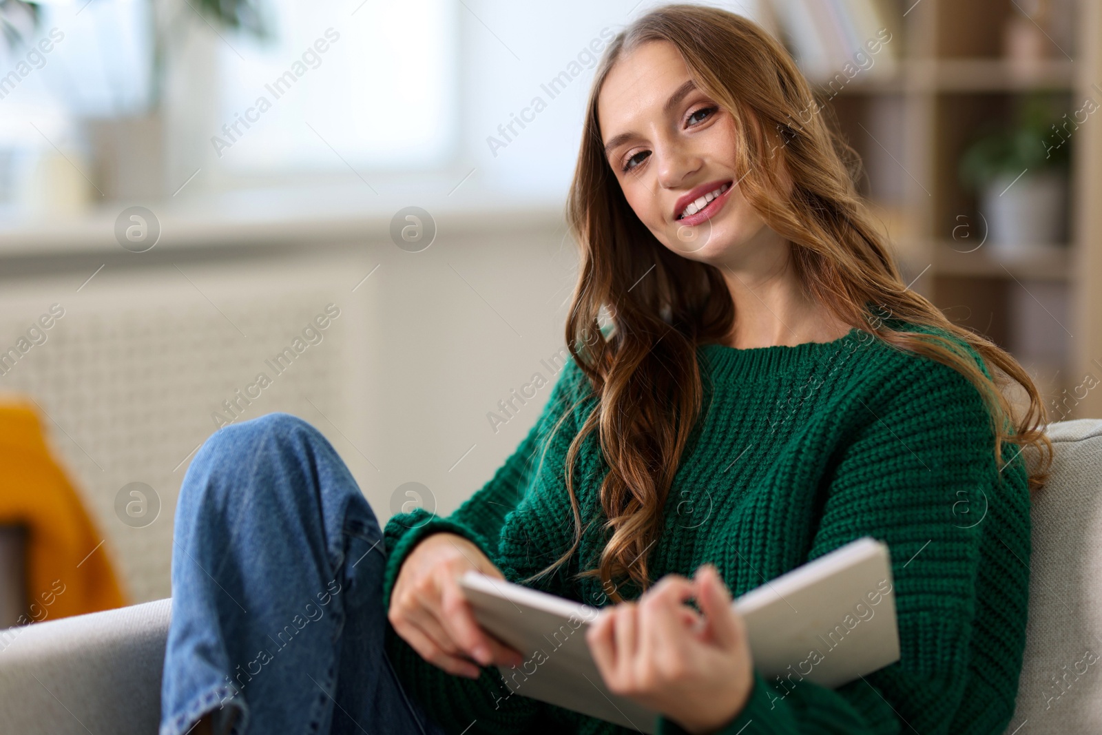 Photo of Charming young woman reading book on sofa at home. Autumn atmosphere