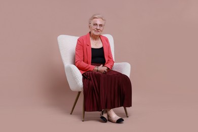 Senior woman in armchair on color background