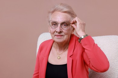 Senior woman in armchair on color background