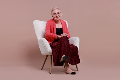 Senior woman in armchair on color background