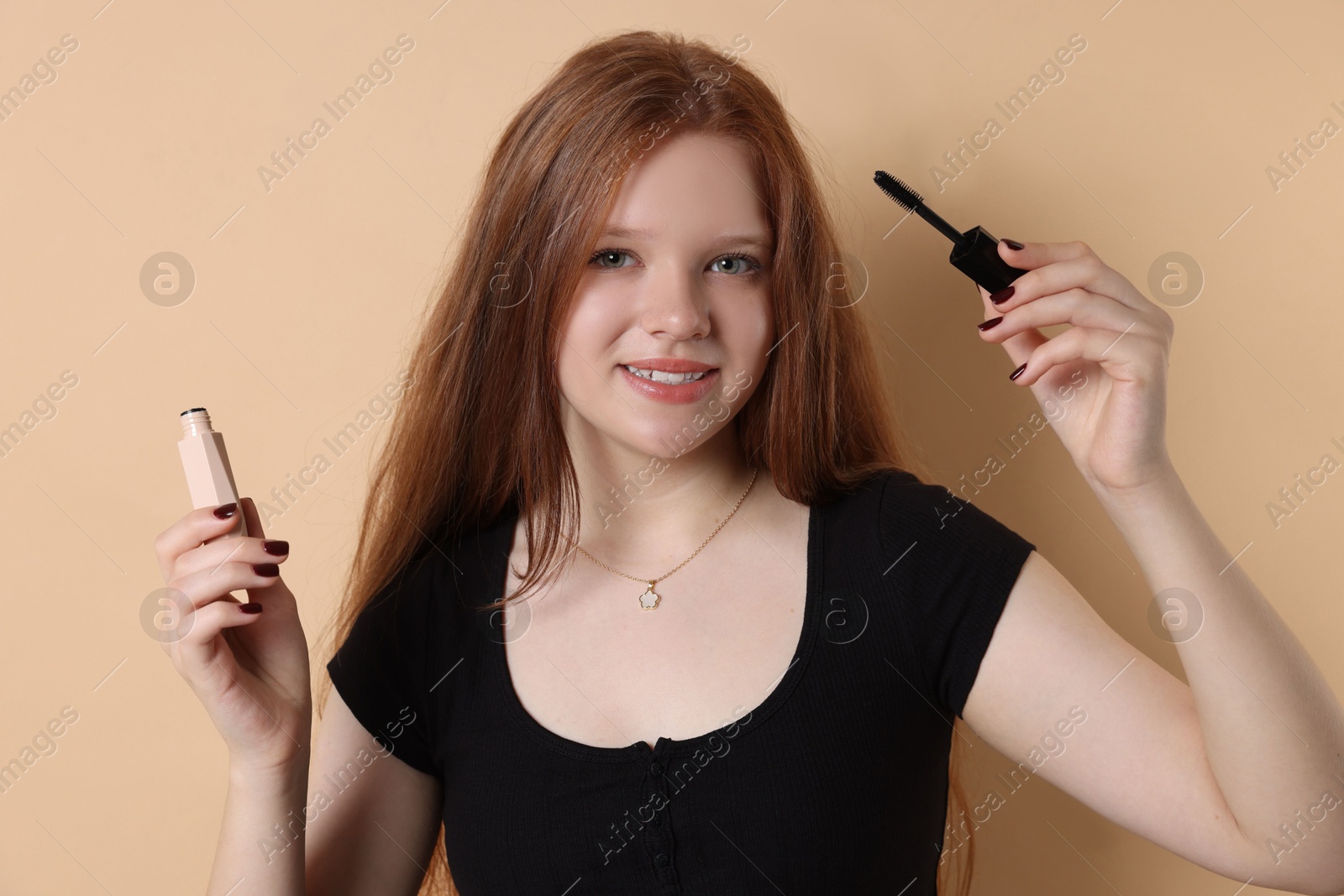 Photo of Smiling teenage girl applying mascara on beige background