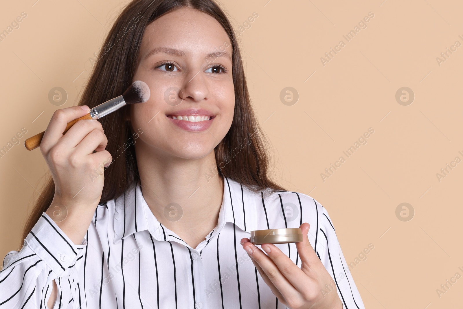 Photo of Smiling teenage girl applying blusher on beige background. Space for text