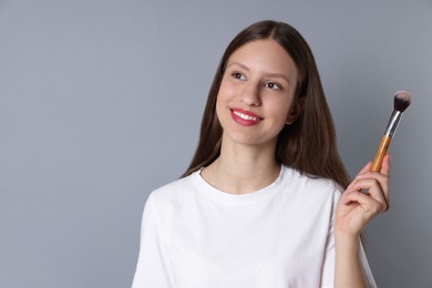 Smiling teenage girl with makeup brush on grey background. Space for text