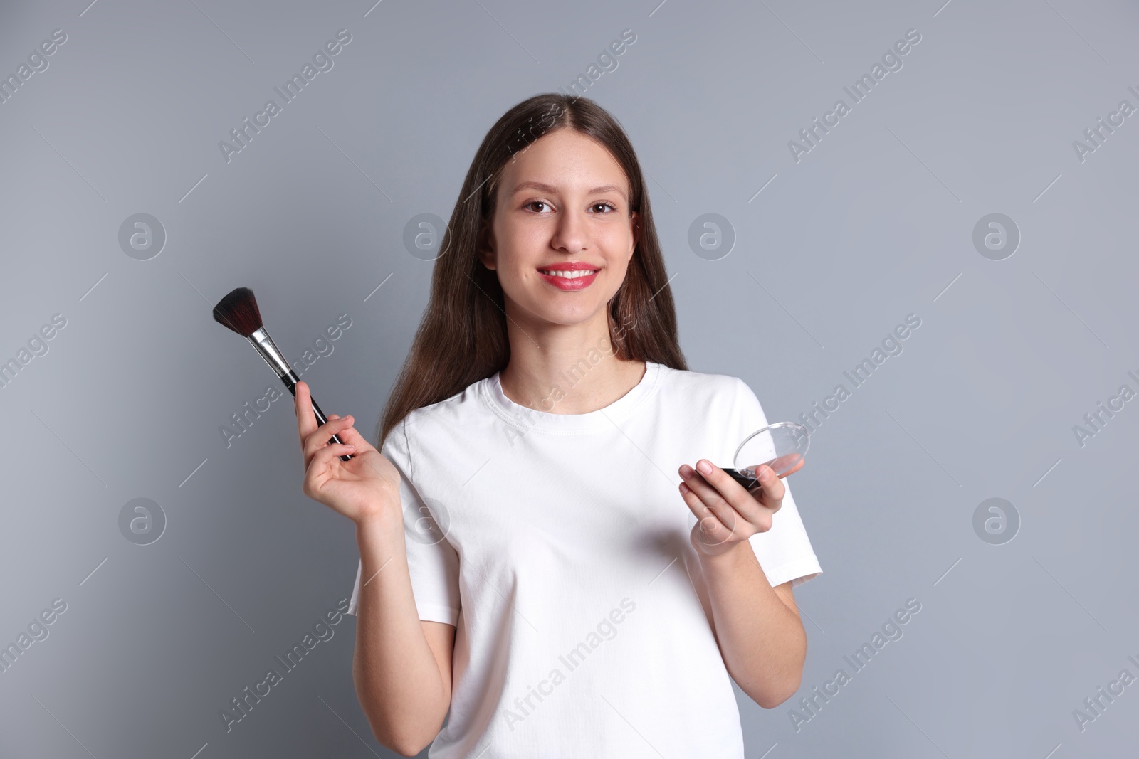 Photo of Smiling teenage girl with blusher and makeup brush on grey background