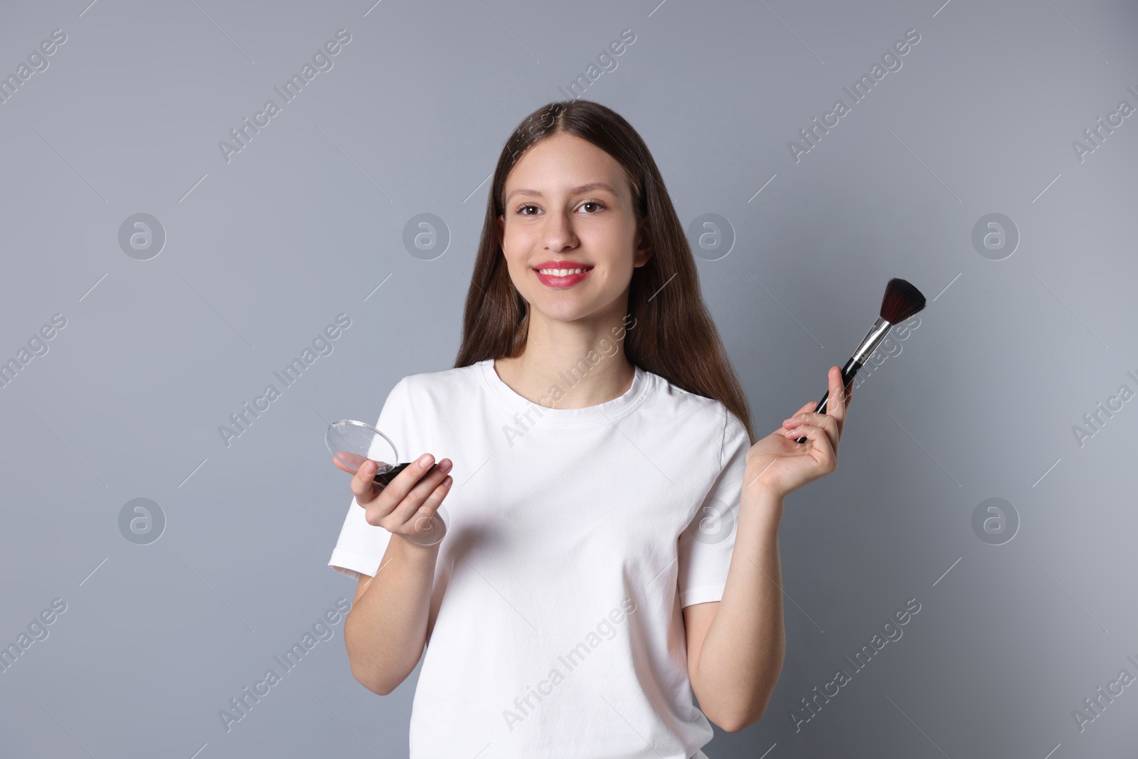 Photo of Smiling teenage girl with blusher and makeup brush on grey background