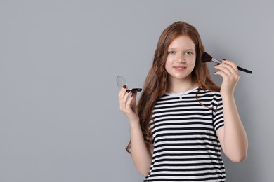 Photo of Smiling teenage girl applying blusher with makeup brush on grey background. Space for text