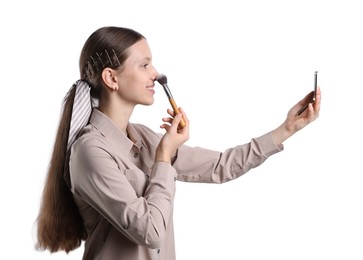 Smiling teenage girl applying blusher with makeup brush on white background