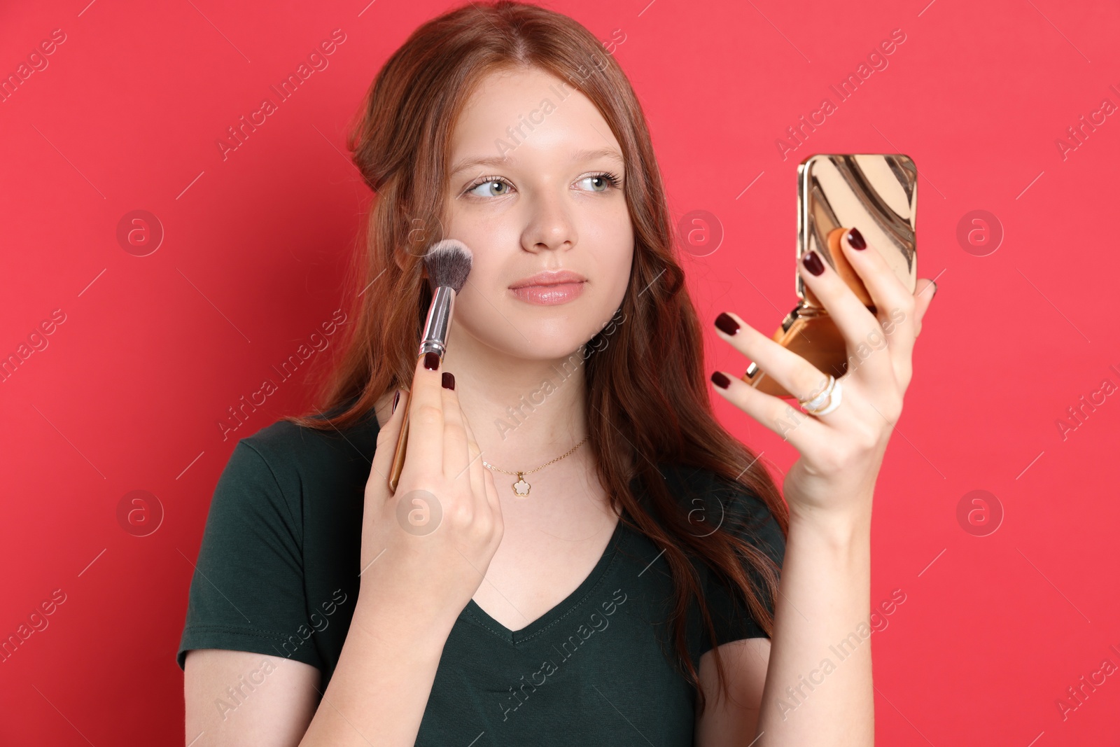 Photo of Teenage girl applying blusher with makeup brush on red background