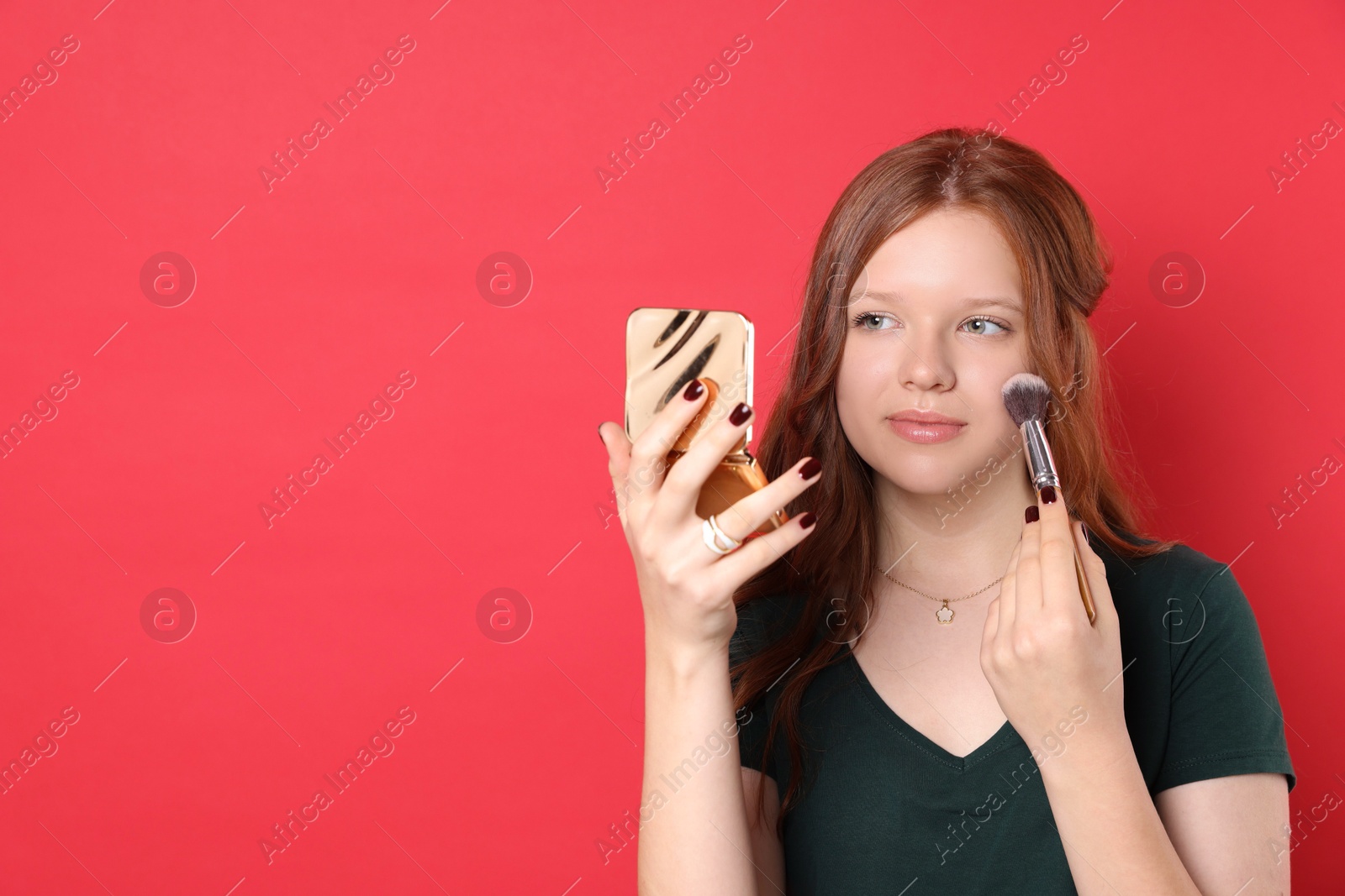 Photo of Teenage girl applying blusher with makeup brush on red background. Space for text