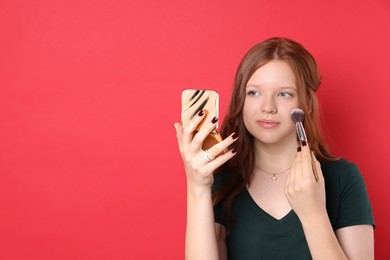 Teenage girl applying blusher with makeup brush on red background. Space for text