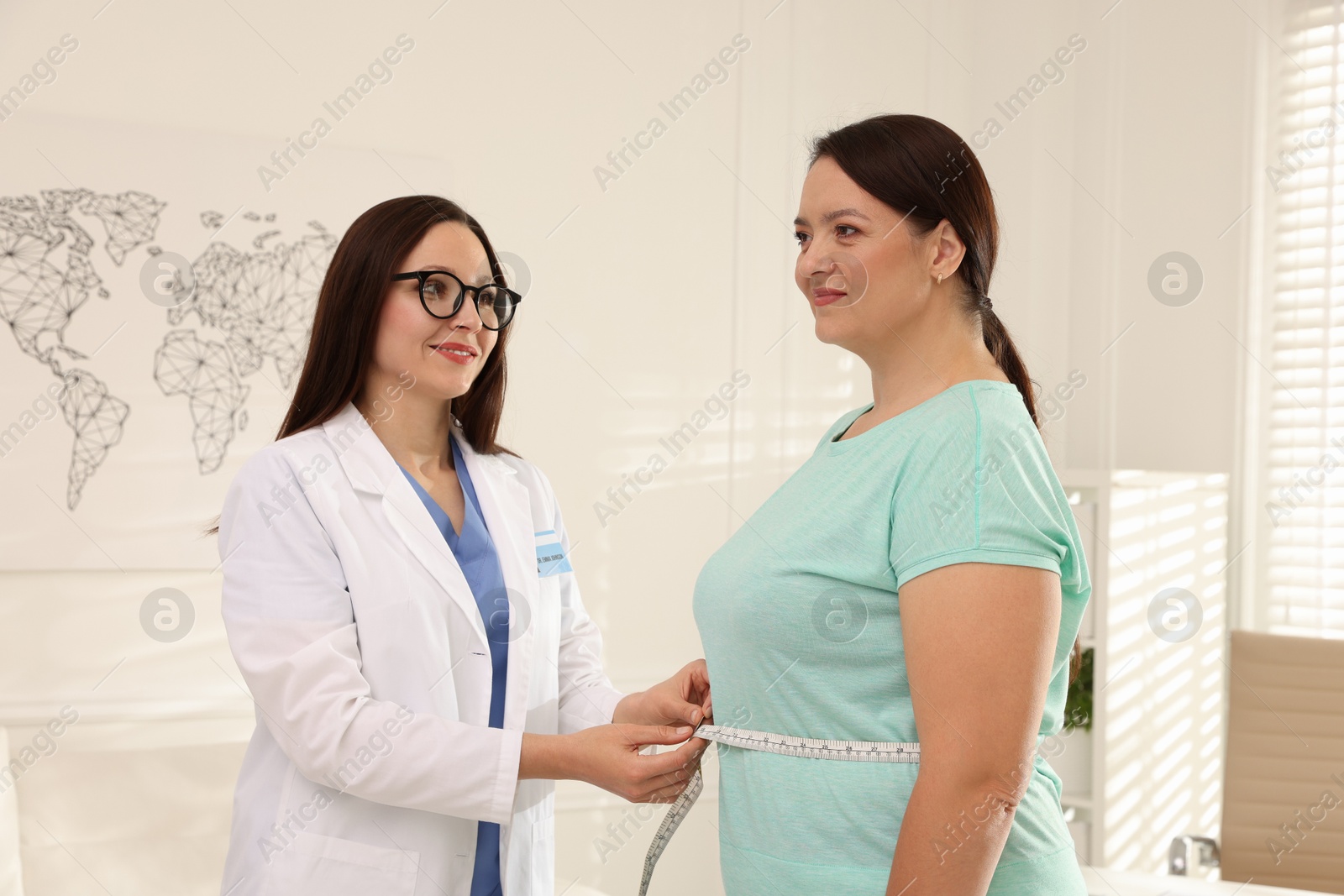 Photo of Nutritionist measuring overweight woman's waist with tape in hospital