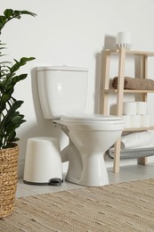 Photo of Ceramic toilet bowl, necessities and houseplant in restroom