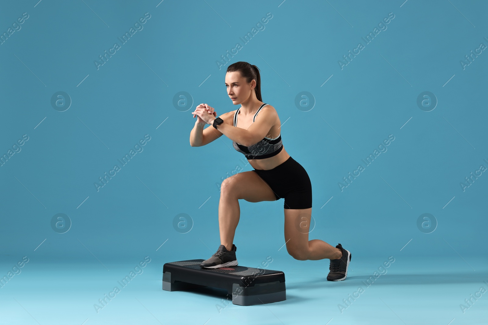 Photo of Woman in gym clothes doing exercise with step platform on light blue background