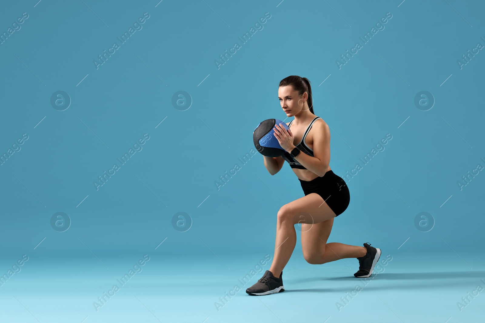 Photo of Woman in gym clothes doing exercise with medicine ball on light blue background