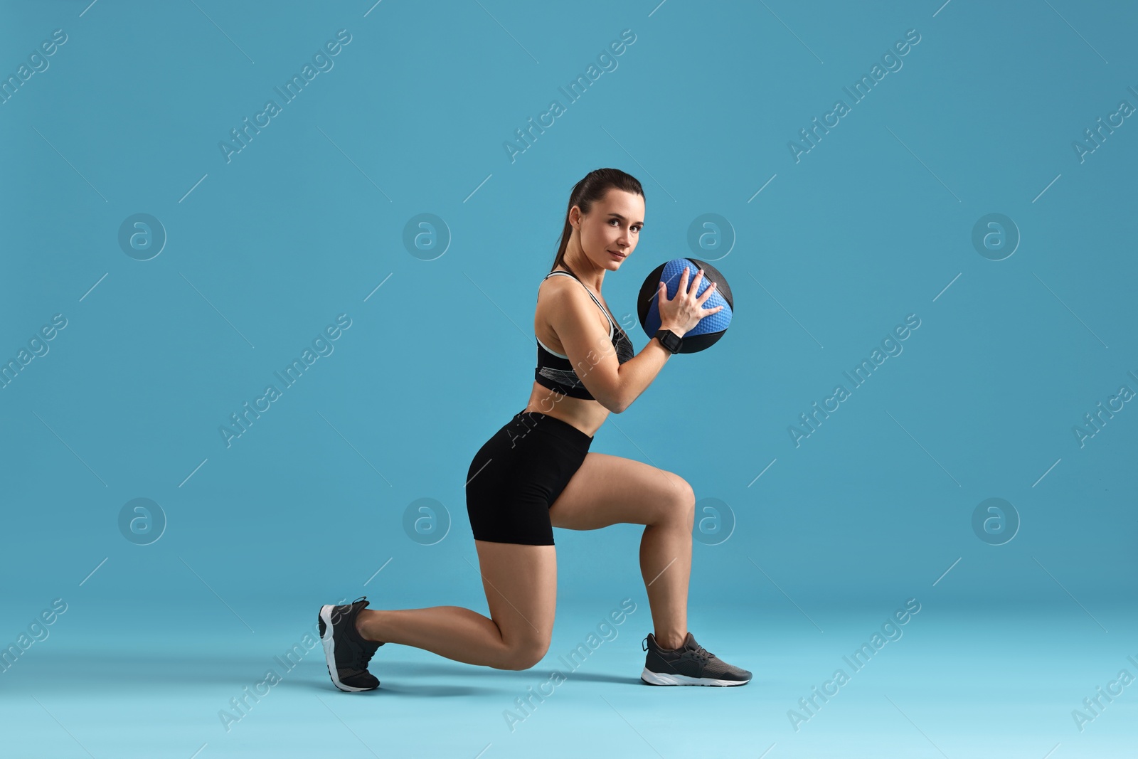 Photo of Woman in gym clothes doing exercise with medicine ball on light blue background