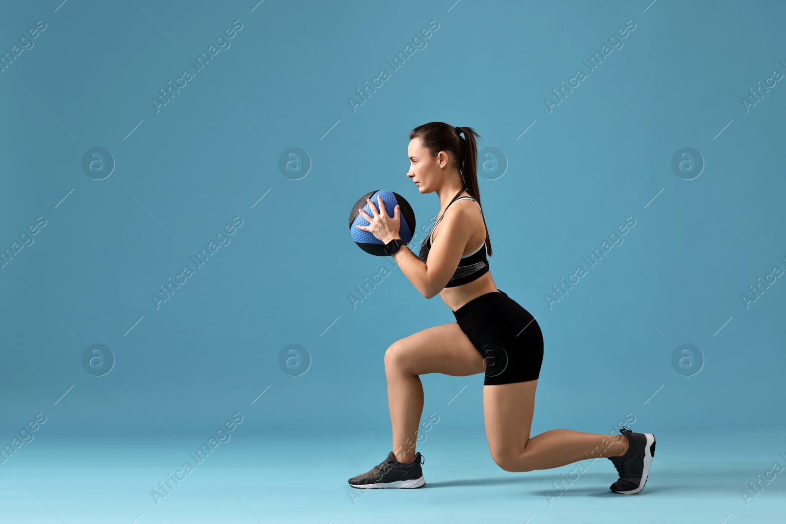 Photo of Woman in gym clothes doing exercise with medicine ball on light blue background