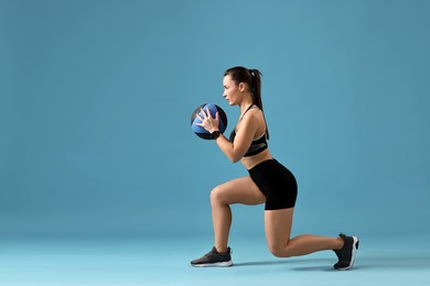 Woman in gym clothes doing exercise with medicine ball on light blue background