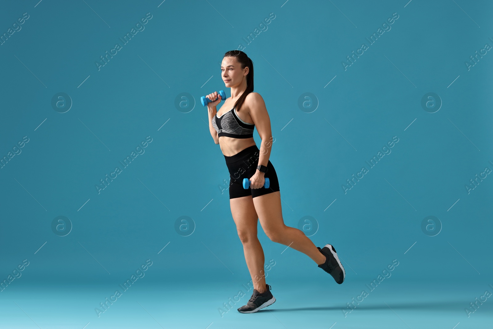 Photo of Woman in gym clothes exercising with dumbbells on light blue background