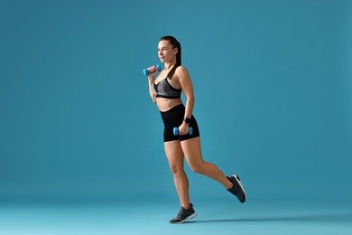 Woman in gym clothes exercising with dumbbells on light blue background