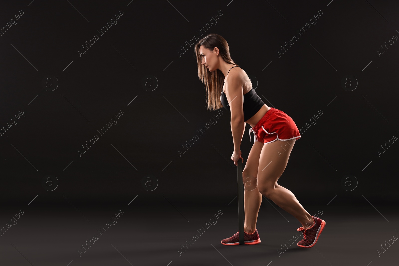 Photo of Woman in gym clothes doing exercise with elastic band on black background