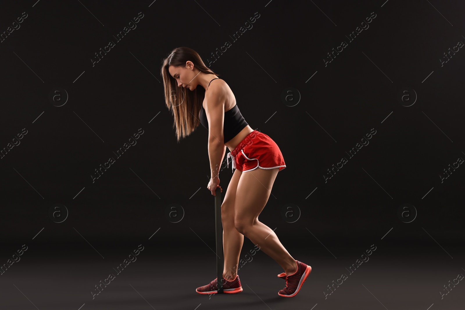 Photo of Woman in gym clothes doing exercise with elastic band on black background