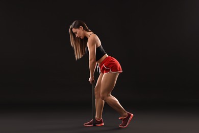 Photo of Woman in gym clothes doing exercise with elastic band on black background