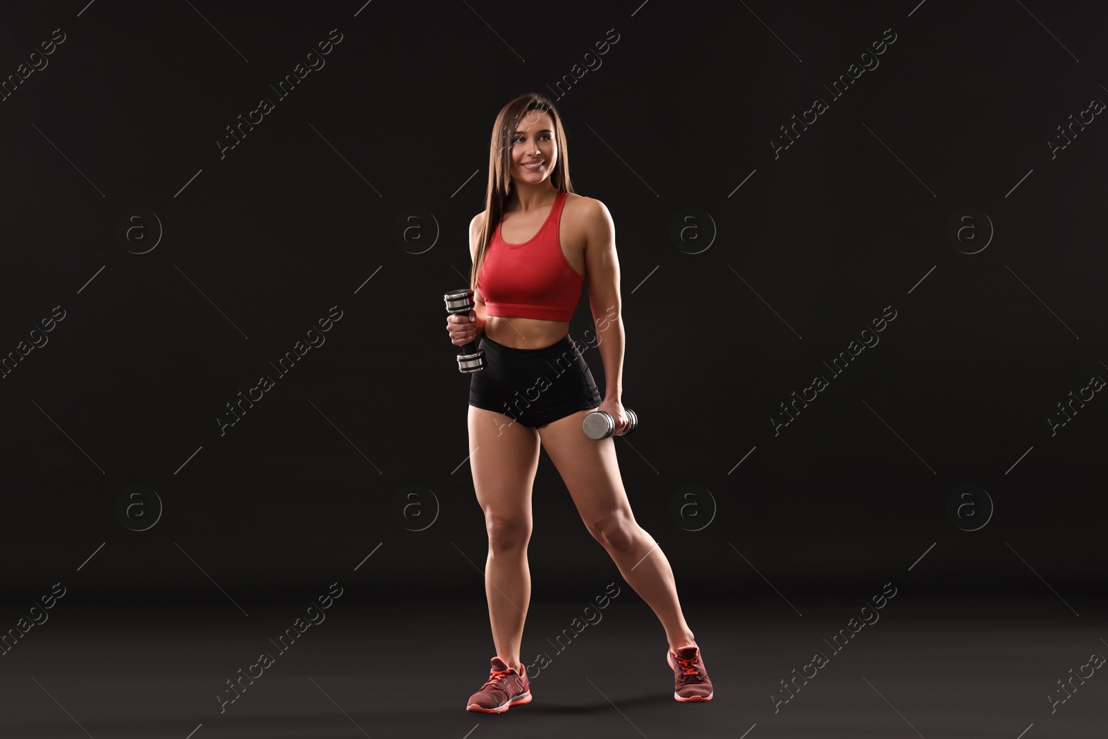 Photo of Woman in gym clothes exercising with dumbbells on black background