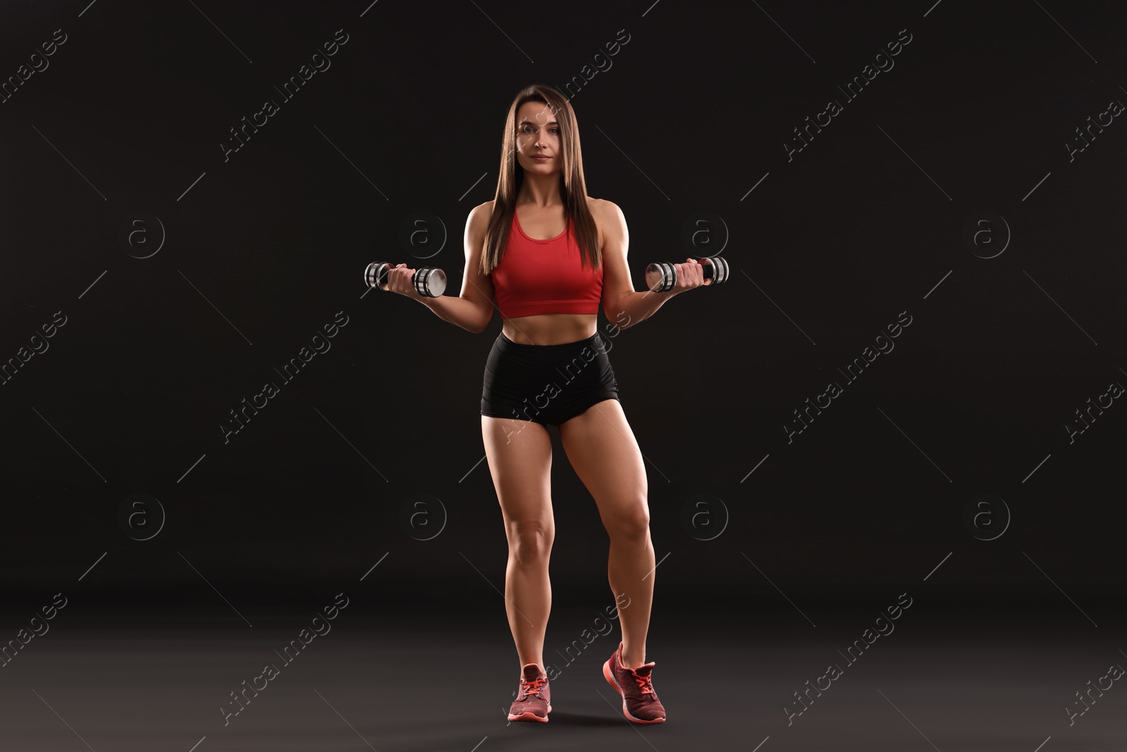 Photo of Woman in gym clothes exercising with dumbbells on black background