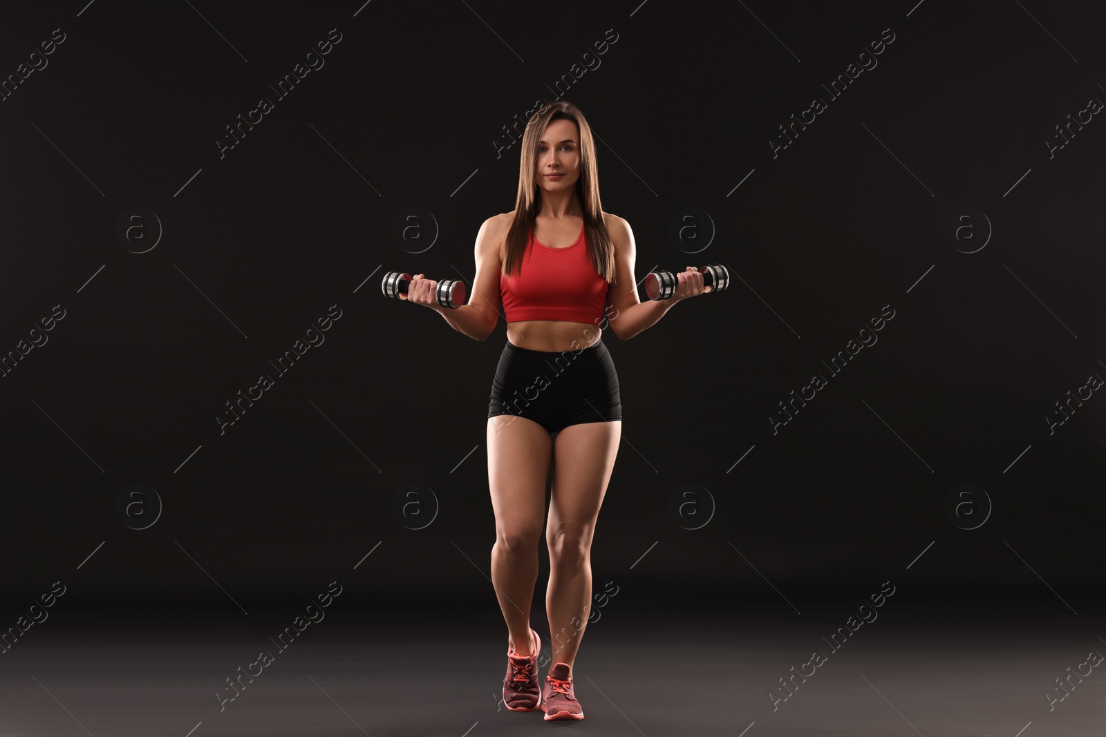 Photo of Woman in gym clothes exercising with dumbbells on black background