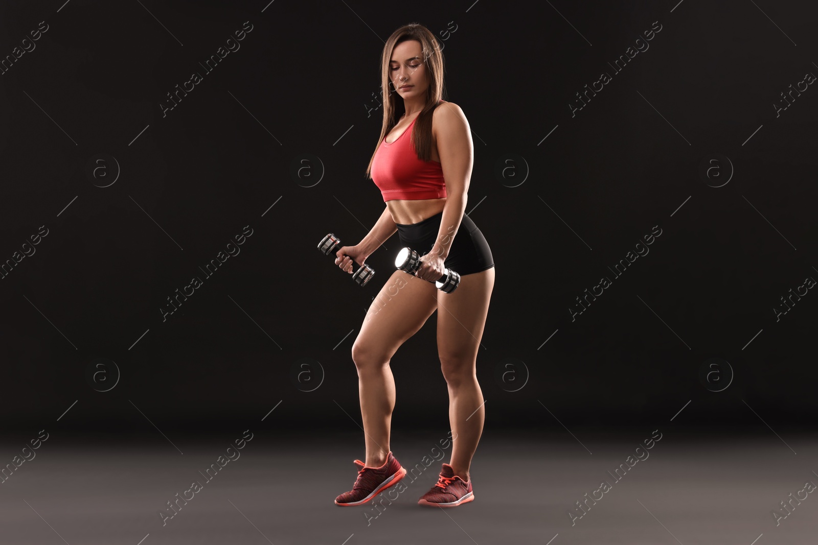 Photo of Woman in gym clothes exercising with dumbbells on black background