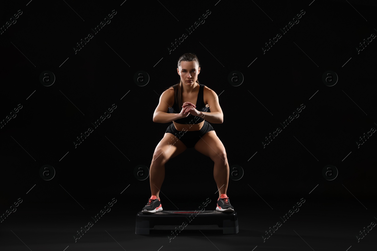 Photo of Beautiful woman in sportswear training on black background